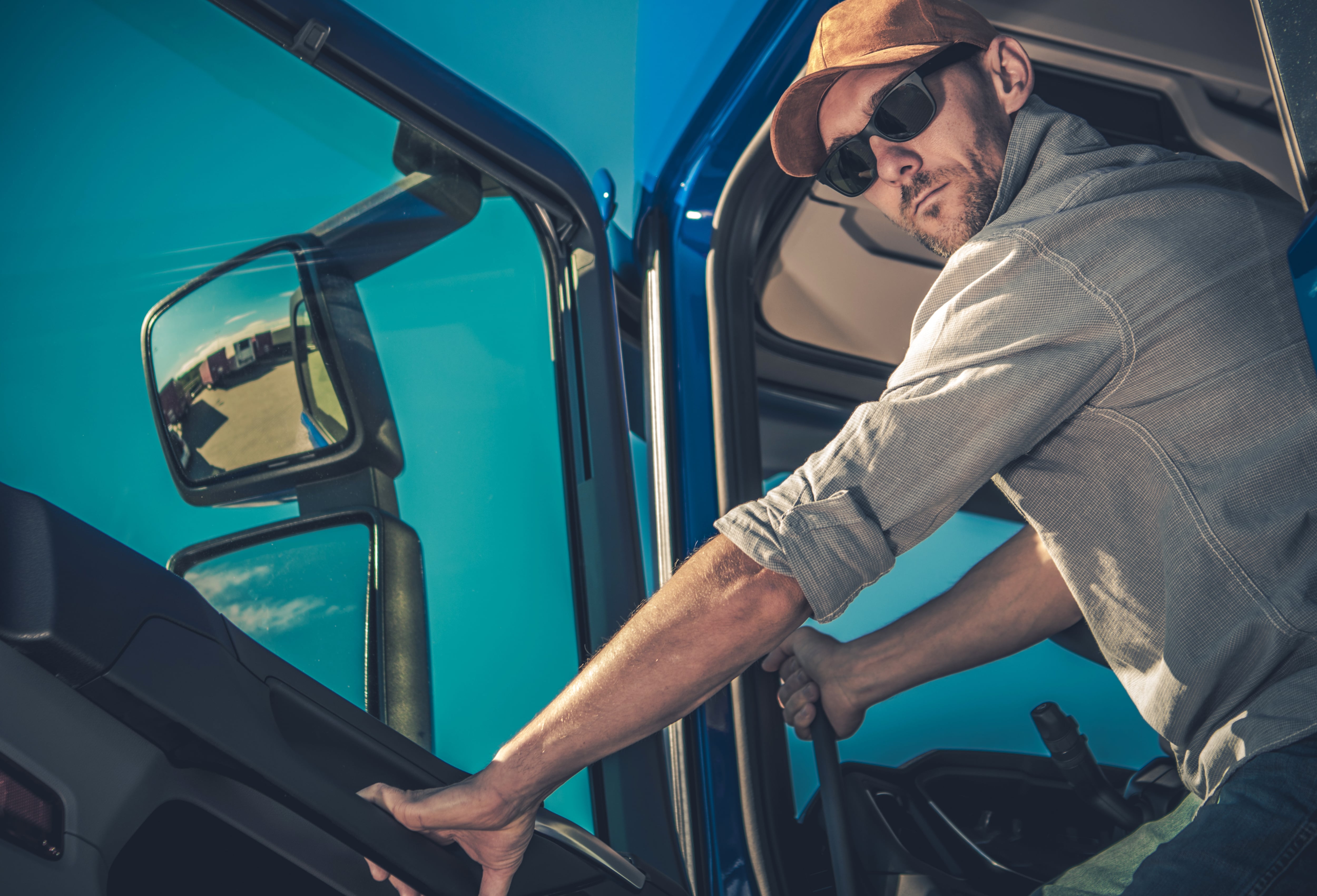 truck driver with hat and sunglasses stands in the doorway of his truck